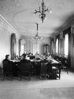 Senaatin talousosaston istunto 26.3. 1917. Vasemmalta pöydän ympärillä: K. Kallio, M. Paasivuori, R. Holsti, J. Ailio, Leo Ehrnrooth, E.N. Setälä, O. Tokoi, A. Serlachius, V. Voionmaa, A. Tulenheimo, V. Tanner ja V. Vuolijoki. Kuva: Museovirasto 53879.